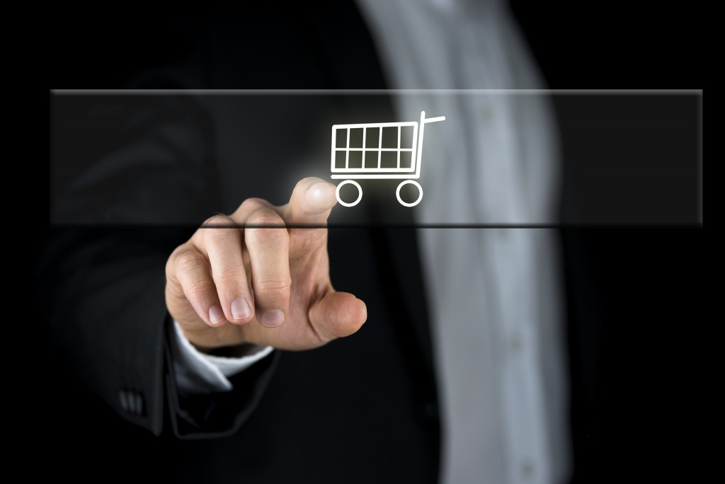 Shopping cart on a navigation bar on a virtual screen or interface with a businessman touching it with his finger from behind in an online shopping and e-commerce concept.